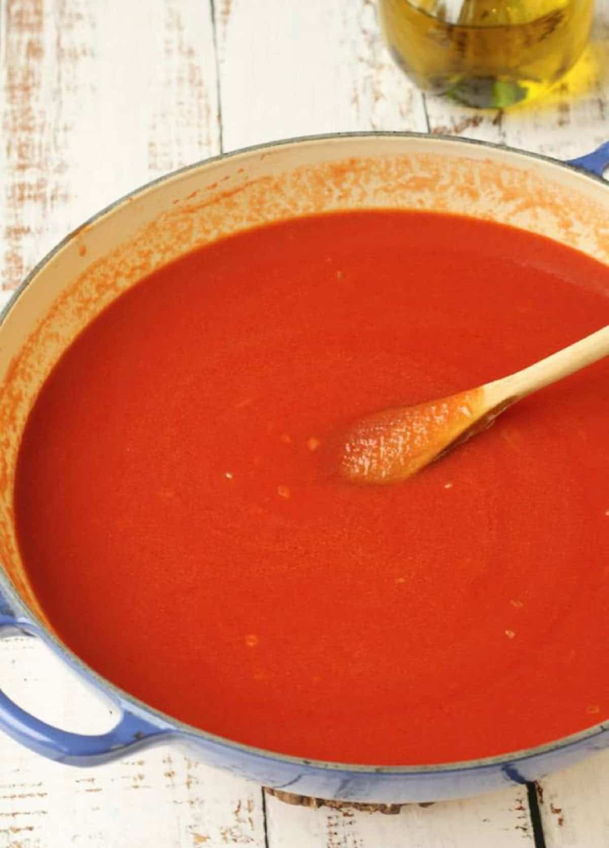 Skillet filled with tomato sauce stirred with wooden spoon for scaccia filling.