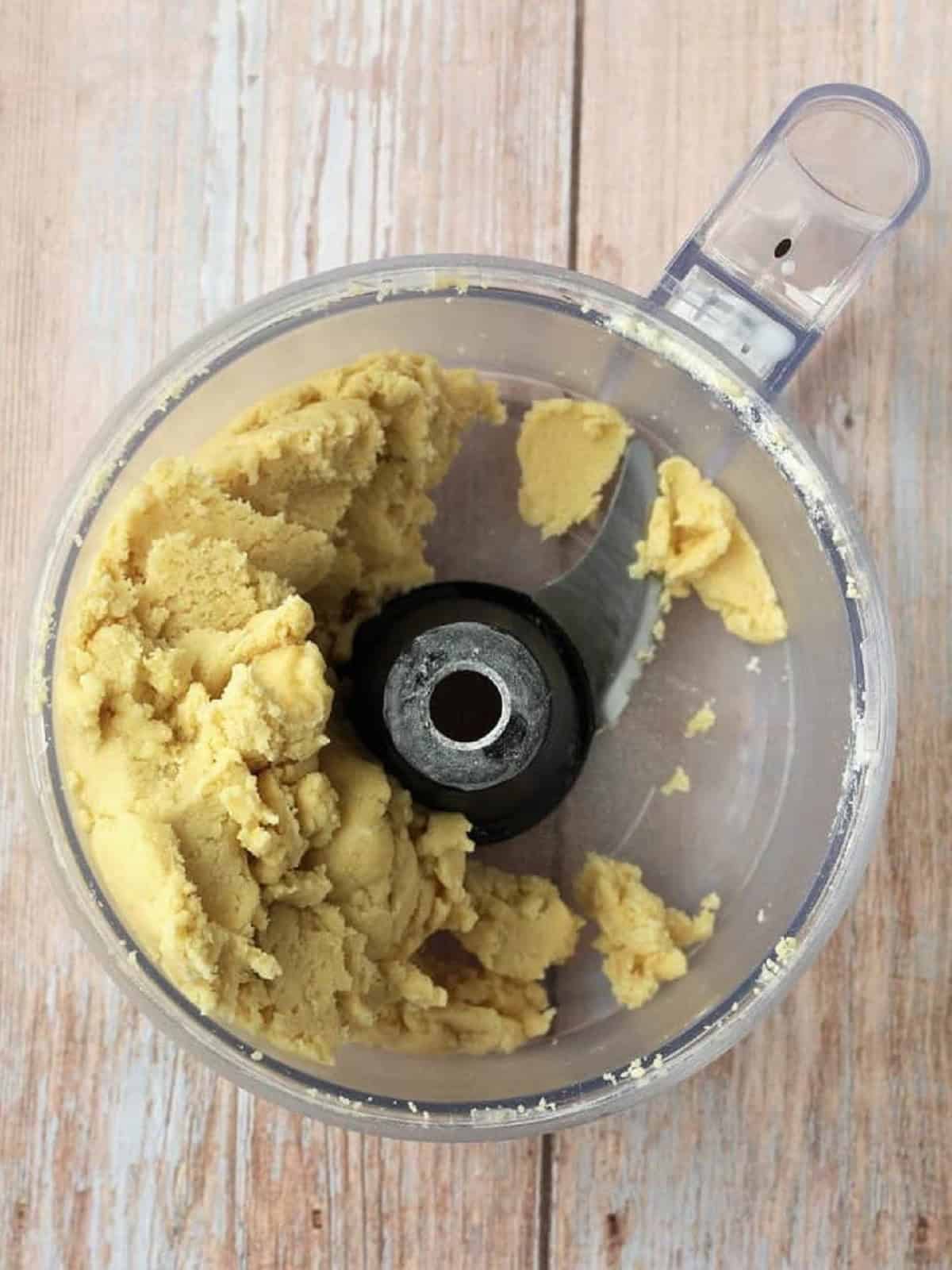 Shortbread dough wrapped around blade in food processor bowl.