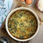 Tortino di bietole e ricotta in round casserole dish surrounded by eggs, bowl of cheese and serving spoon.