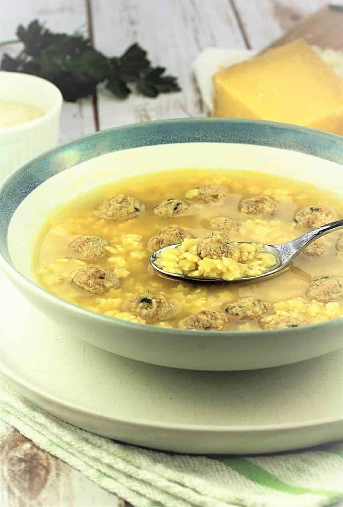 Italian chicken soup with meatballs in bowl with spoon.