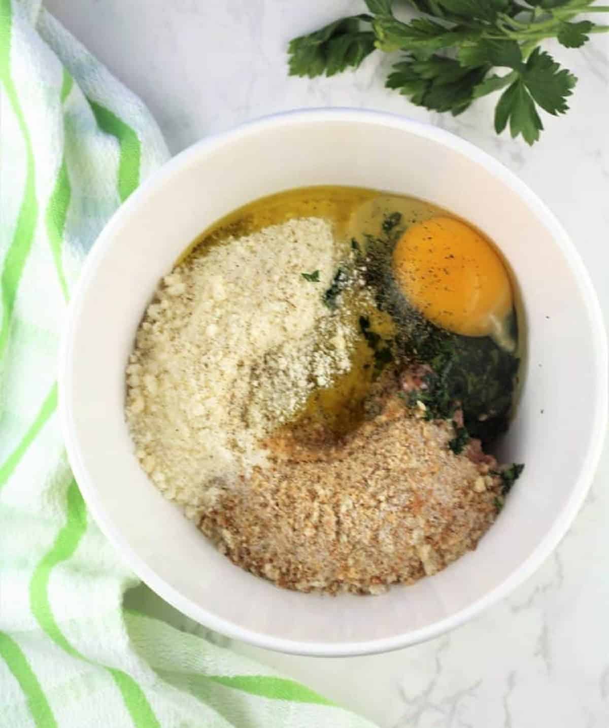 Bowl with ground meat, egg, breadcrumbs, cheese and parsley for tiny meatballs.