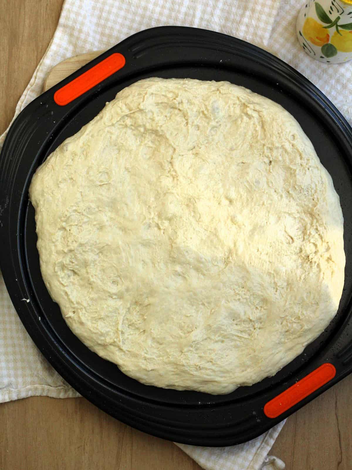 No knead pizza dough spread on pizza pan.