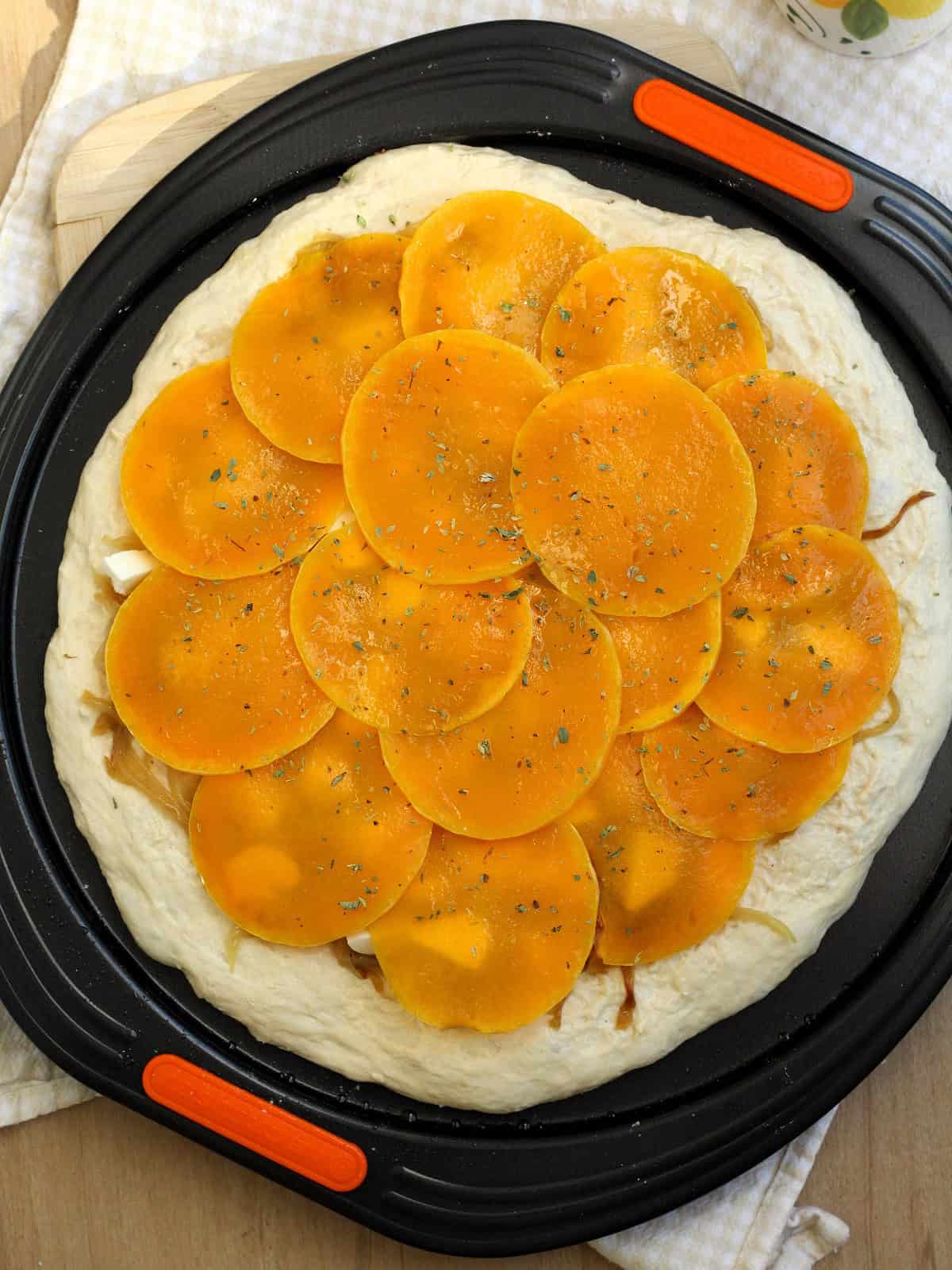 Pizza dough topped with butternut squash rounds on pizza pan.