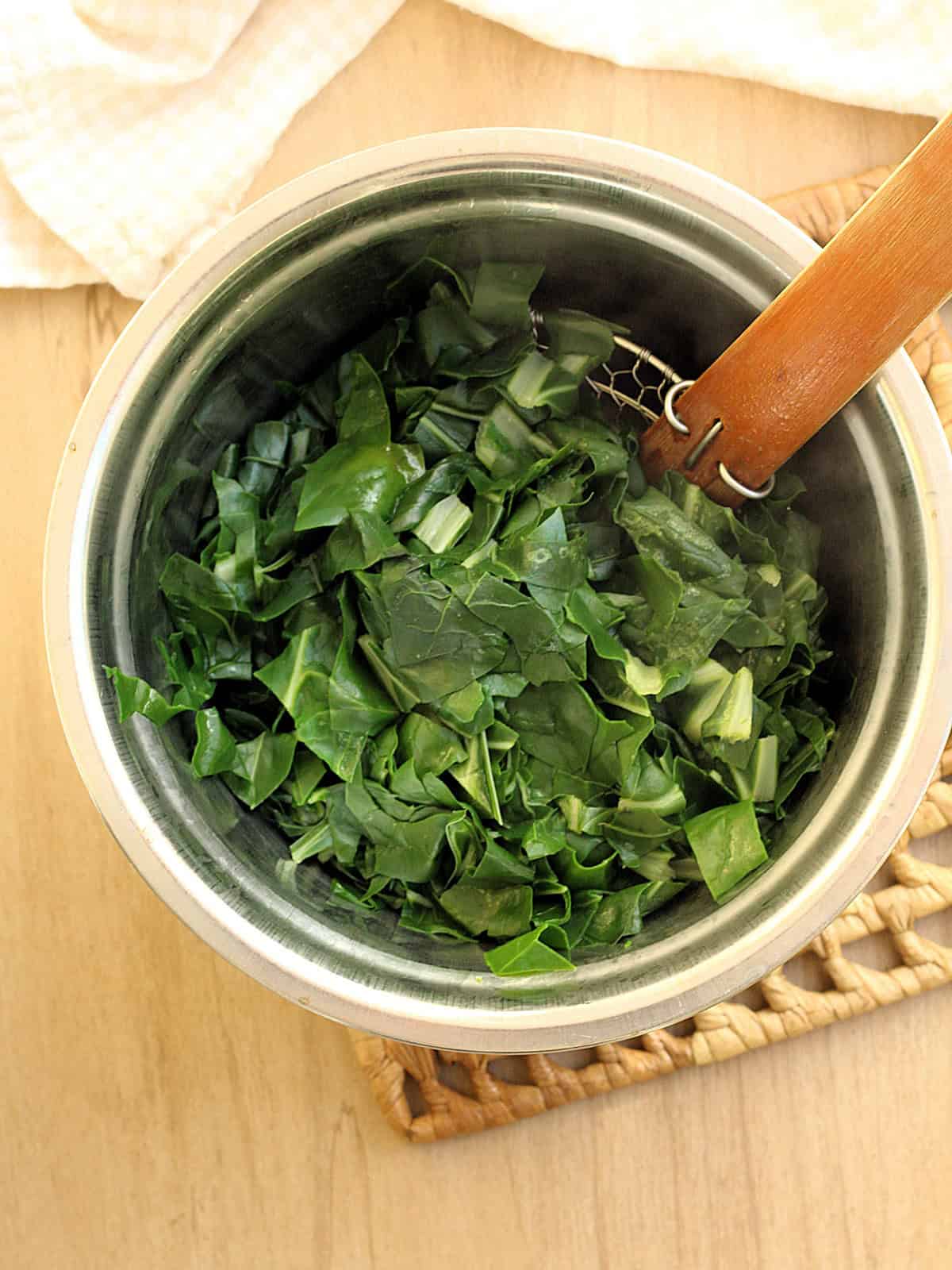Boiled swiss chard drained in spider over bowl.