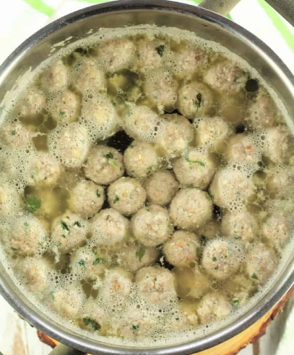Tiny meatballs simmering in chicken broth in sauce pan.