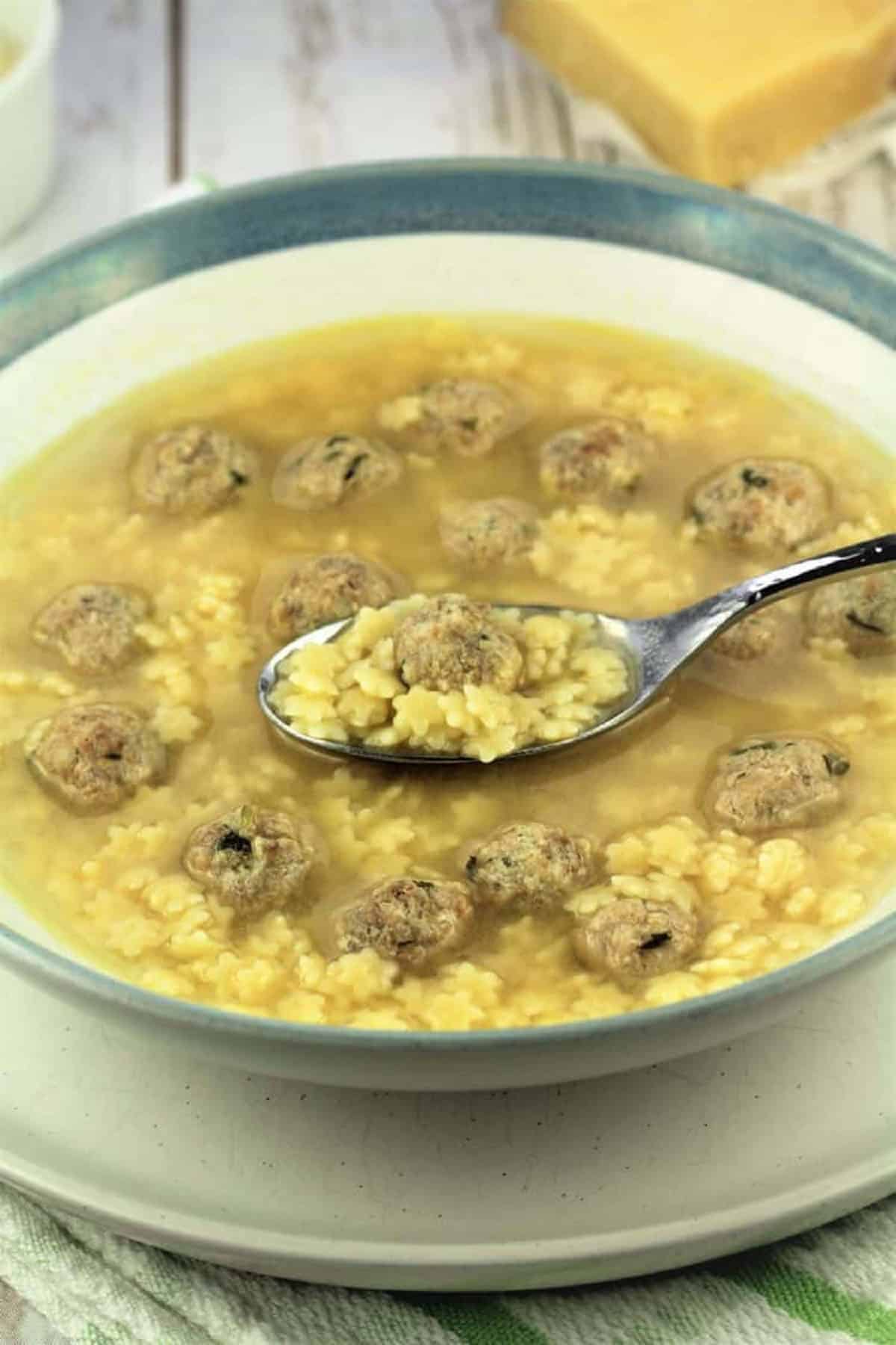 Spoonful of pastina soup with tiny meatballs taken from bowl full of soup.